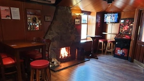 A bar area with a stone fireplace, wooden flooring, red bar stools, and a television screen. - COMMERCIAL HOTEL (Alness)