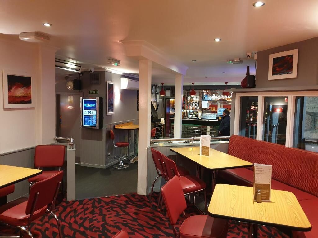 A restaurant with red chairs and tables, a bar area, and a digital menu display.
