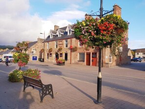 A street with a bench, a building with flower baskets, and a sign that reads 'Hotel.' - COMMERCIAL HOTEL (Alness)