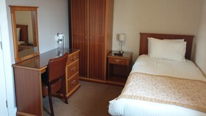 A hotel room with a bed, a desk with a chair, a wardrobe, and a nightstand with a lamp. - COMMERCIAL HOTEL (Alness)