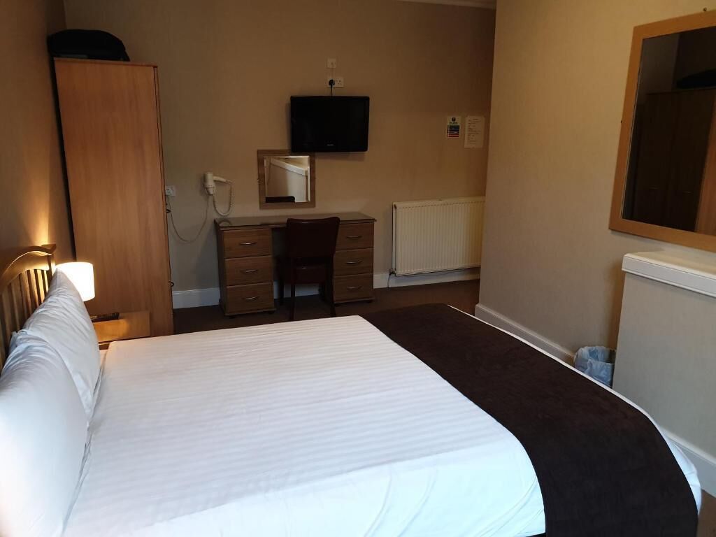 A hotel room with a bed, a desk, a chair, a wardrobe, a television, and a mirror.