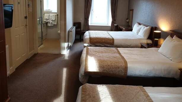 A hotel room with two beds, a TV, a bathroom with a shower, and a window with curtains. - COMMERCIAL HOTEL (Alness)