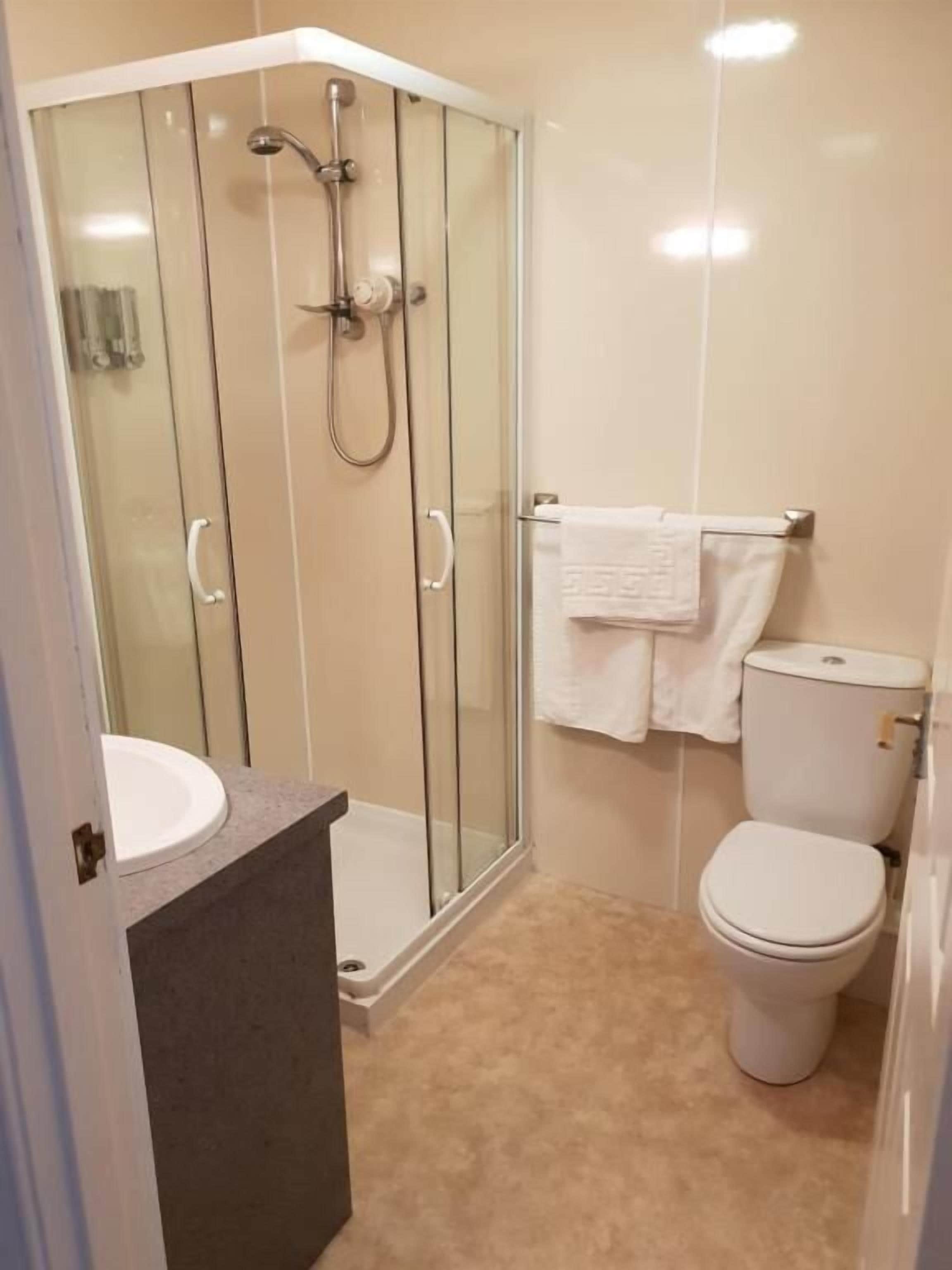 Un baño con ducha de vidrio, inodoro blanco y lavamanos.