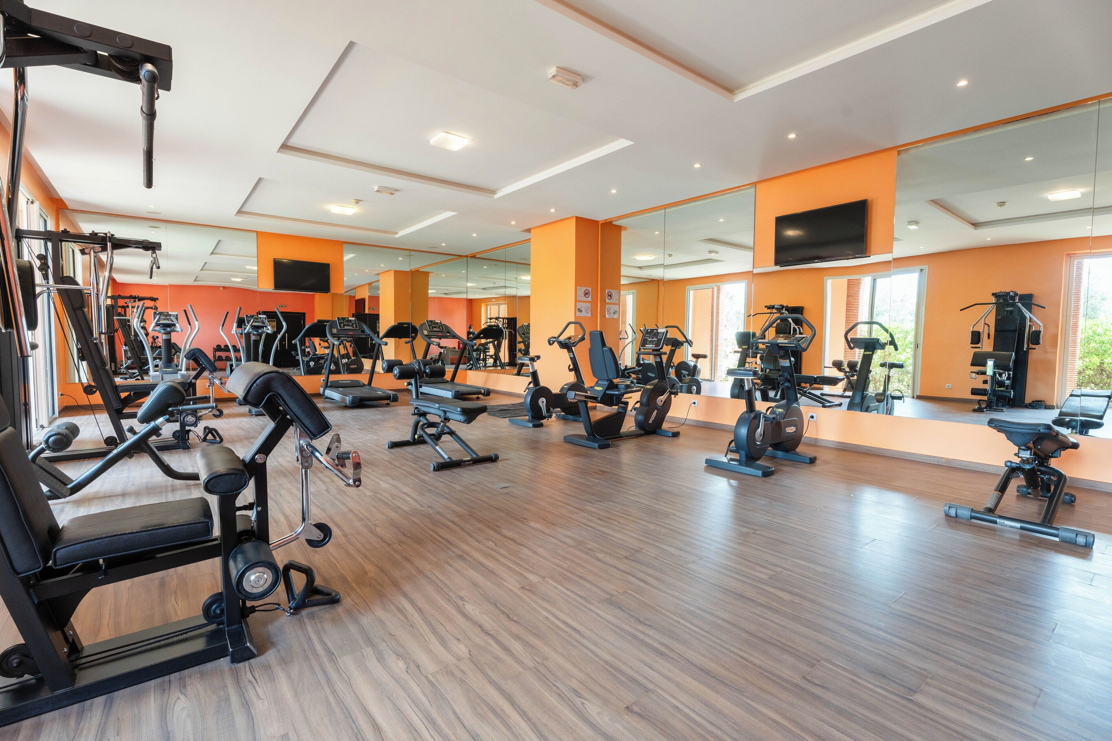 A gym with various exercise equipment, large mirrors, and a wooden floor.