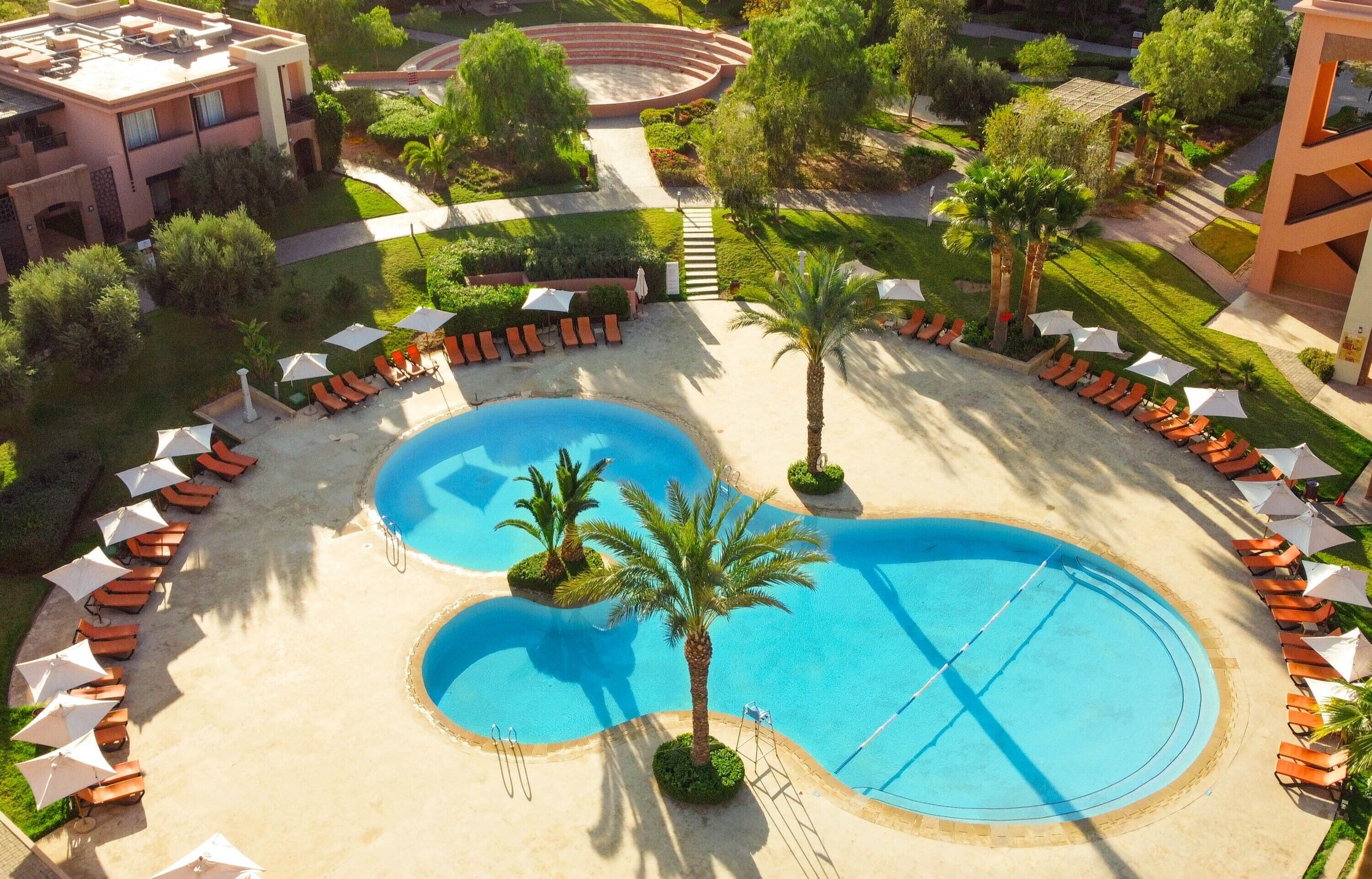 Ett semesterhotell med en pool i mitten, solstolar och palmer.