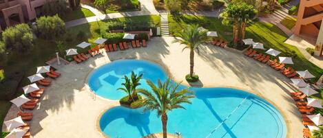 Ein Resort mit einem zentral gelegenen Pool, Liegestühlen und Palmen.