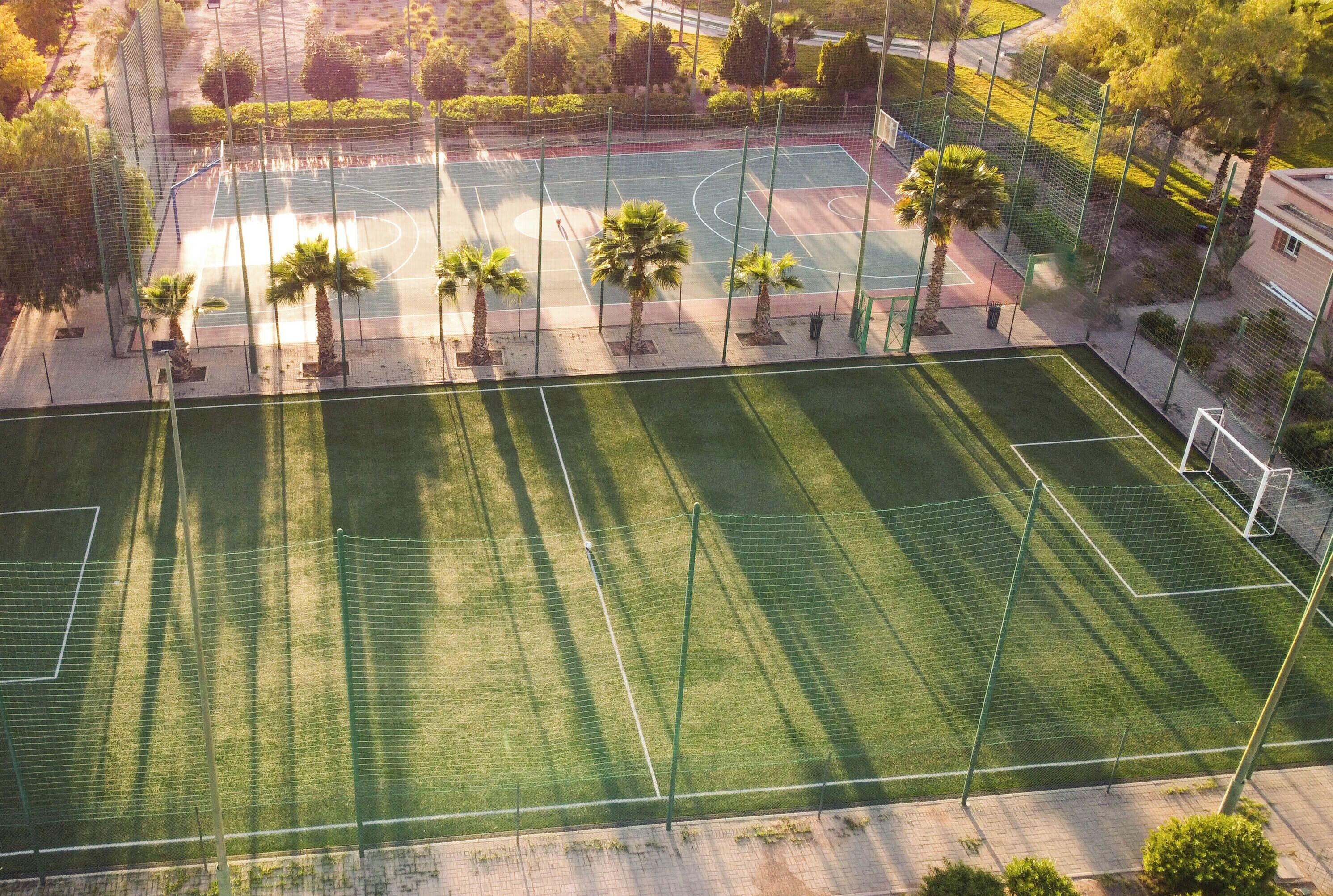 An aerial view of a sports court with surrounding greenery and a fence.