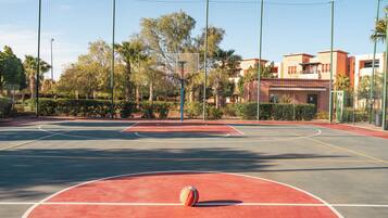 An outdoor basketball court with a netted enclosure, surrounded by trees and buildings.