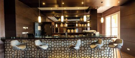 A modern bar area with a patterned wall, hanging pendant lights, and bar stools.