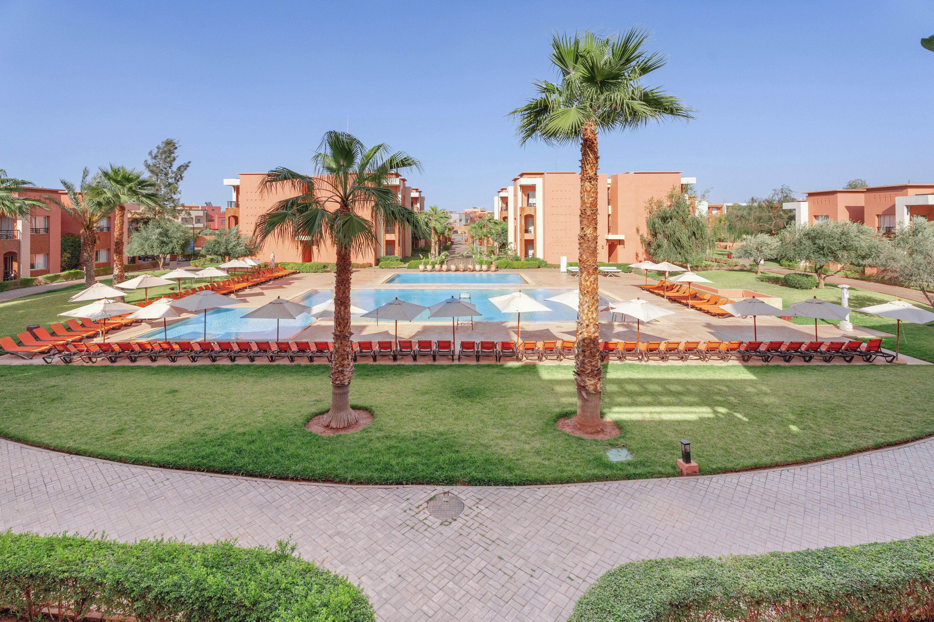 A pool area with lounge chairs and umbrellas, surrounded by palm trees and buildings.