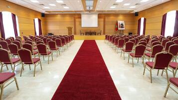 A conference room with rows of red chairs, a red carpet, and a projector screen at the front.