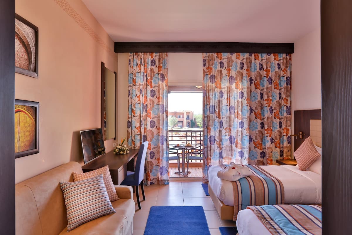 A hotel room with a bed, a sofa, a desk, and a balcony with curtains.