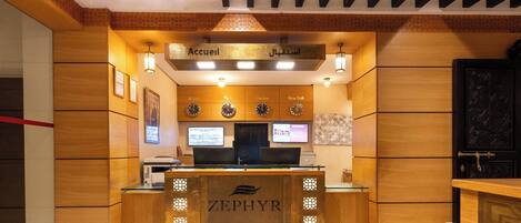 A reception desk with a wooden finish and the name "ZEPHYR" on it. There are two computer monitors above the desk, and a sign above them that reads "Accueil" and "Accueil."