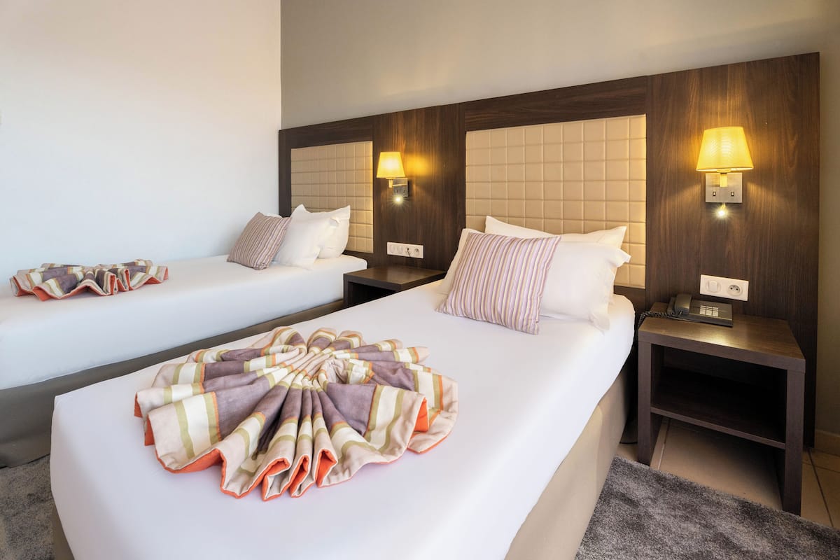 A hotel room with two beds, a large decorative blanket on the left bed, and two bedside lamps.