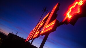 A series of illuminated signs with a star-like design against a twilight sky.