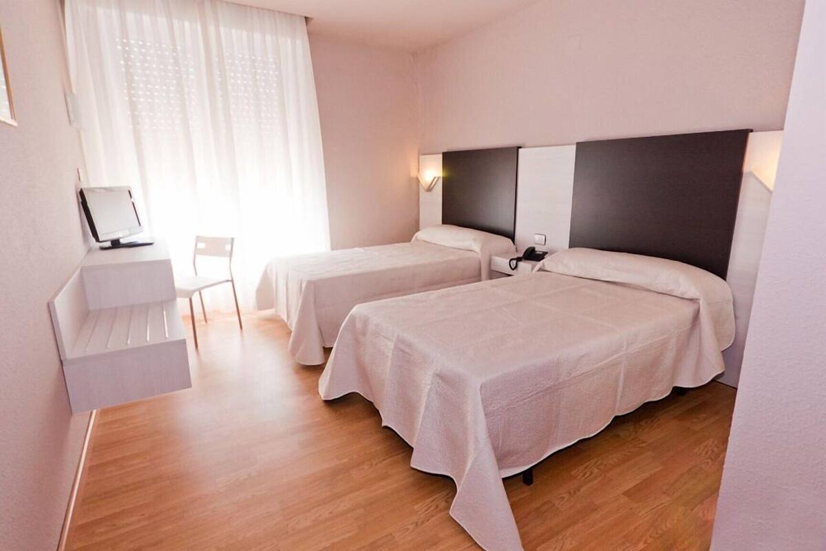 A hotel room with two beds, a desk with a computer, a chair, and a window with curtains.
