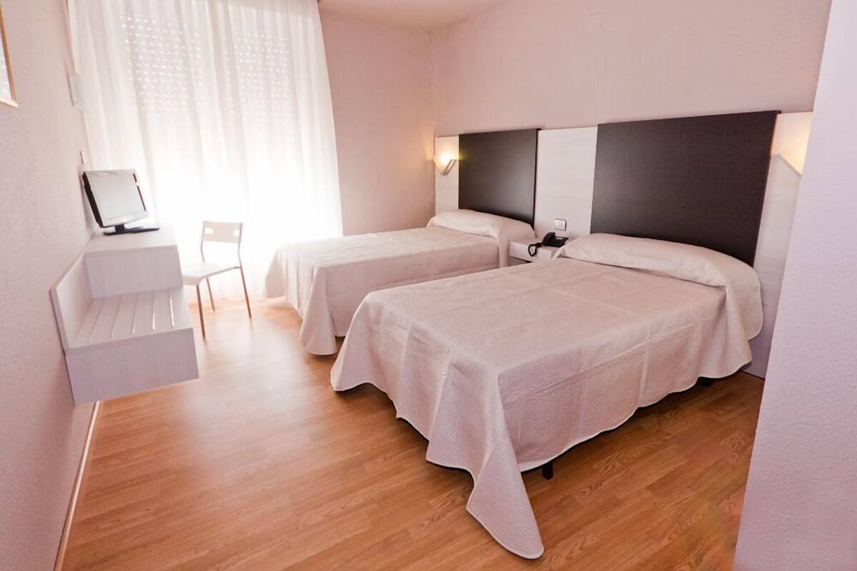 A hotel room with two beds, a desk with a computer, and a chair.