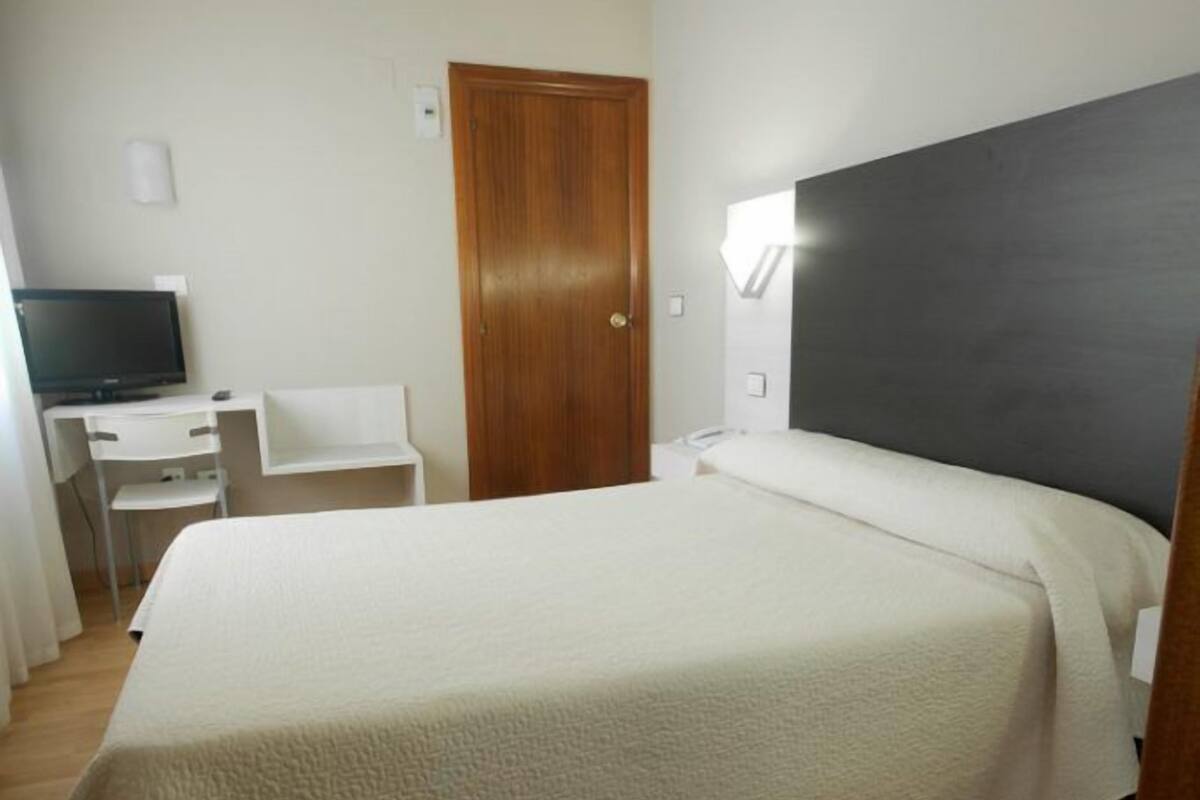 A bedroom with a bed, a desk, a chair, and a television.