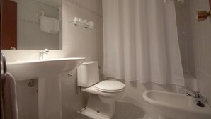 A bathroom with a sink, toilet, bidet, and a shower curtain.