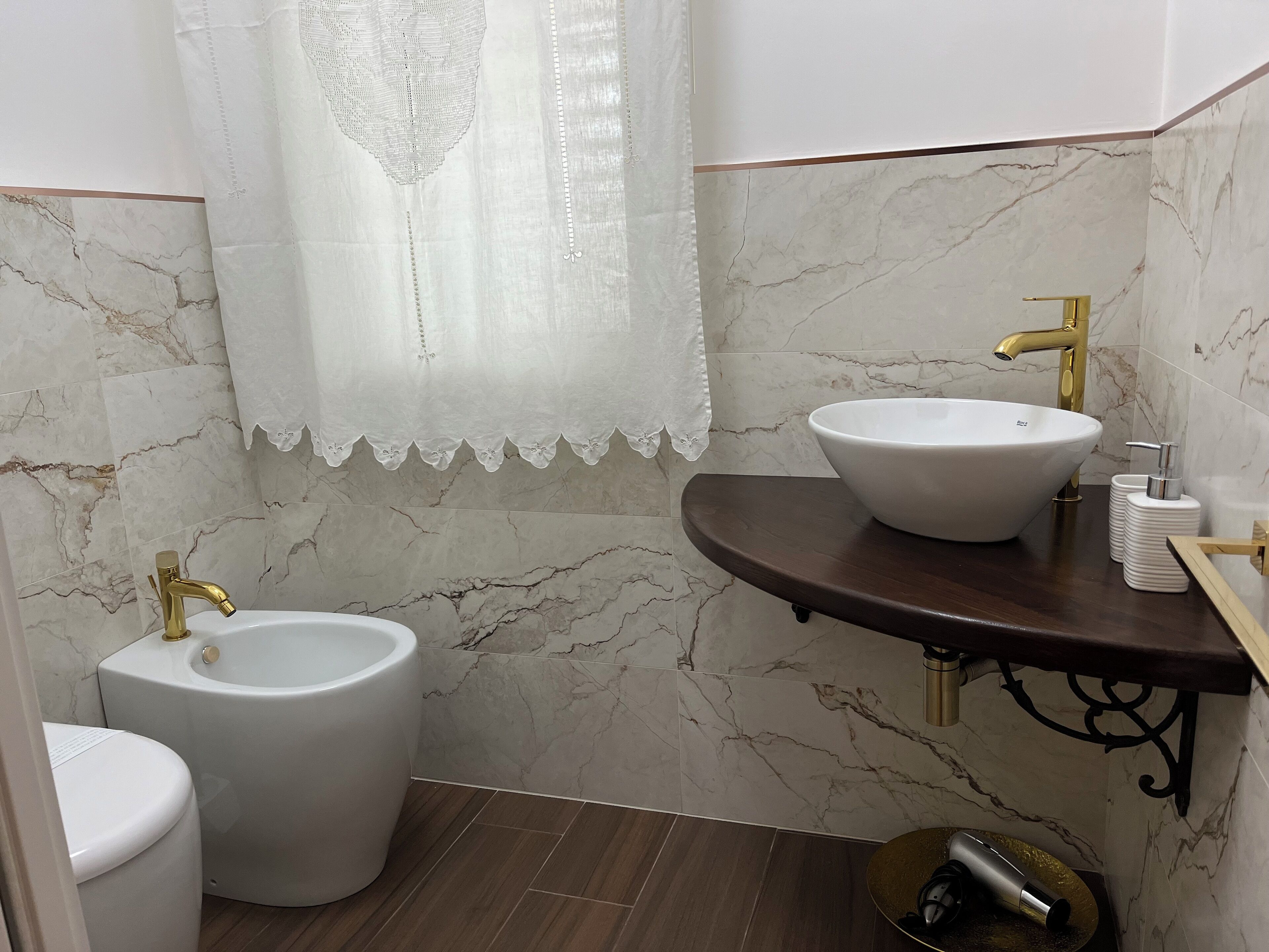 Ein Badezimmer mit einem weißen Waschbecken, einem goldfarbenen Wasserhahn und einer Toilette.