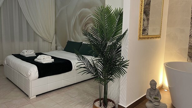 Un dormitorio moderno con una cama, una planta grande en maceta, una estatua de Buda y un espejo montado en la pared.