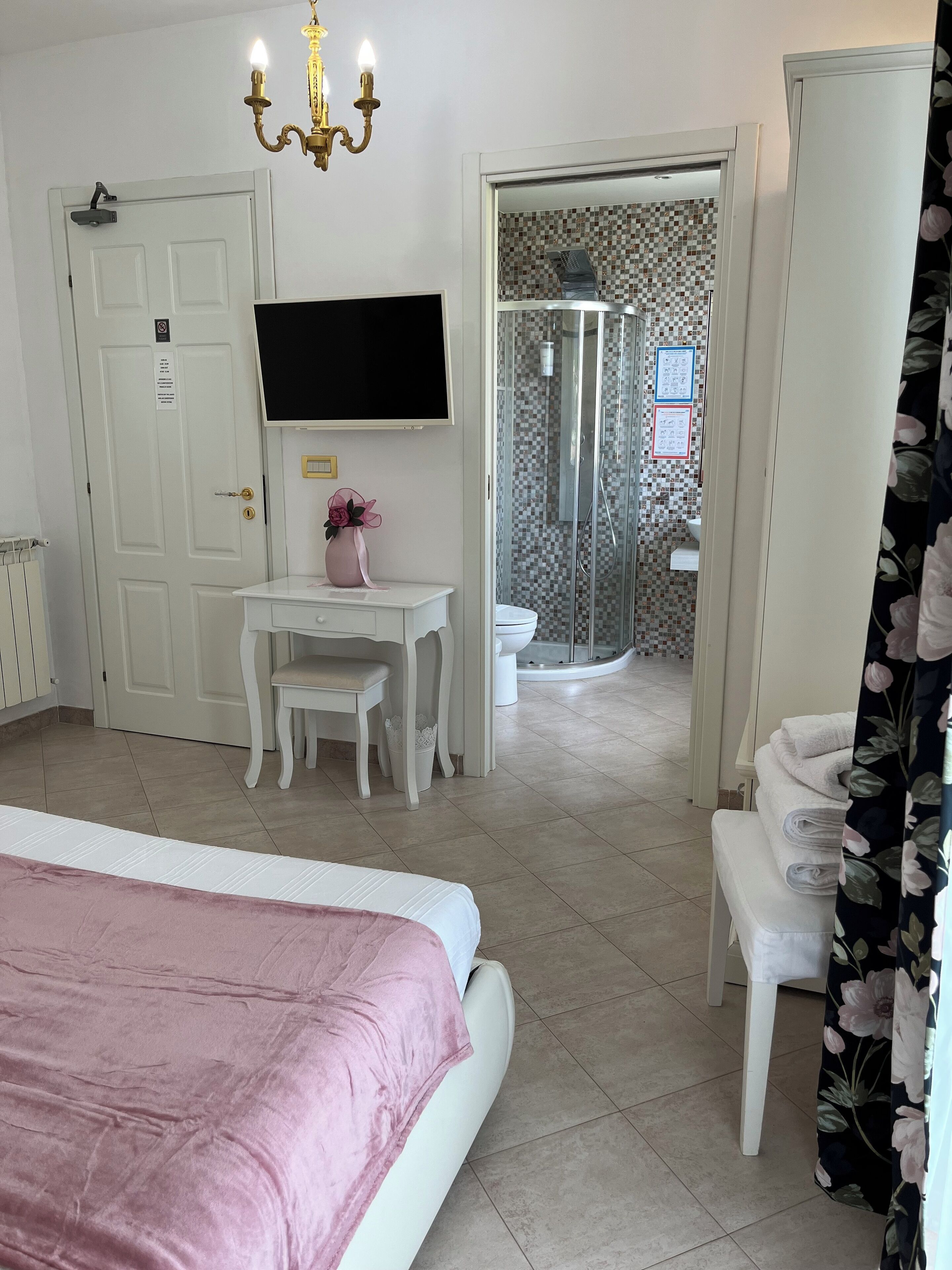 Habitación de hotel con cama, escritorio, silla, zona de ducha y televisor montado en la pared.