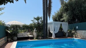 Una piscina rectangular con agua azul cristalina, rodeada por un muro de piedra y una terraza de madera.