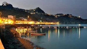 Un pueblo costero al anochecer con edificios iluminados, agua tranquila y barcos.