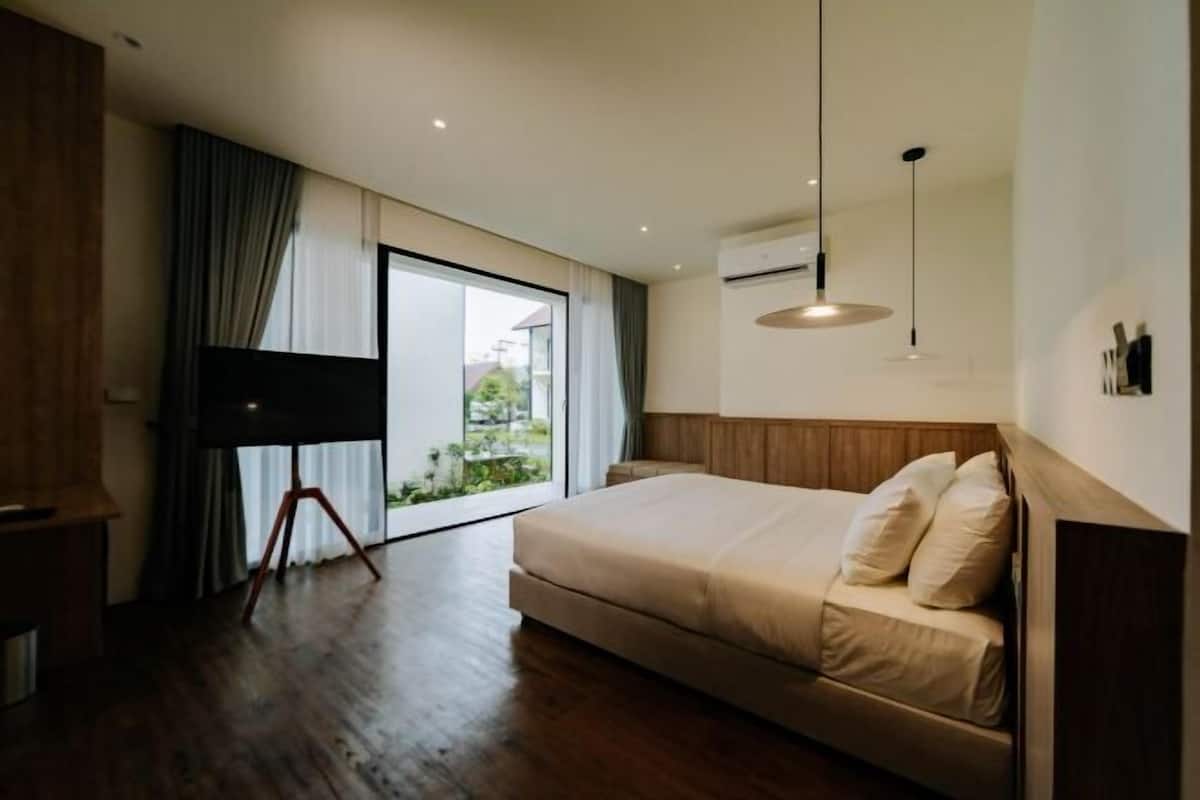 A bedroom with a large bed, a flat-screen TV, and a sliding glass door to the outside.