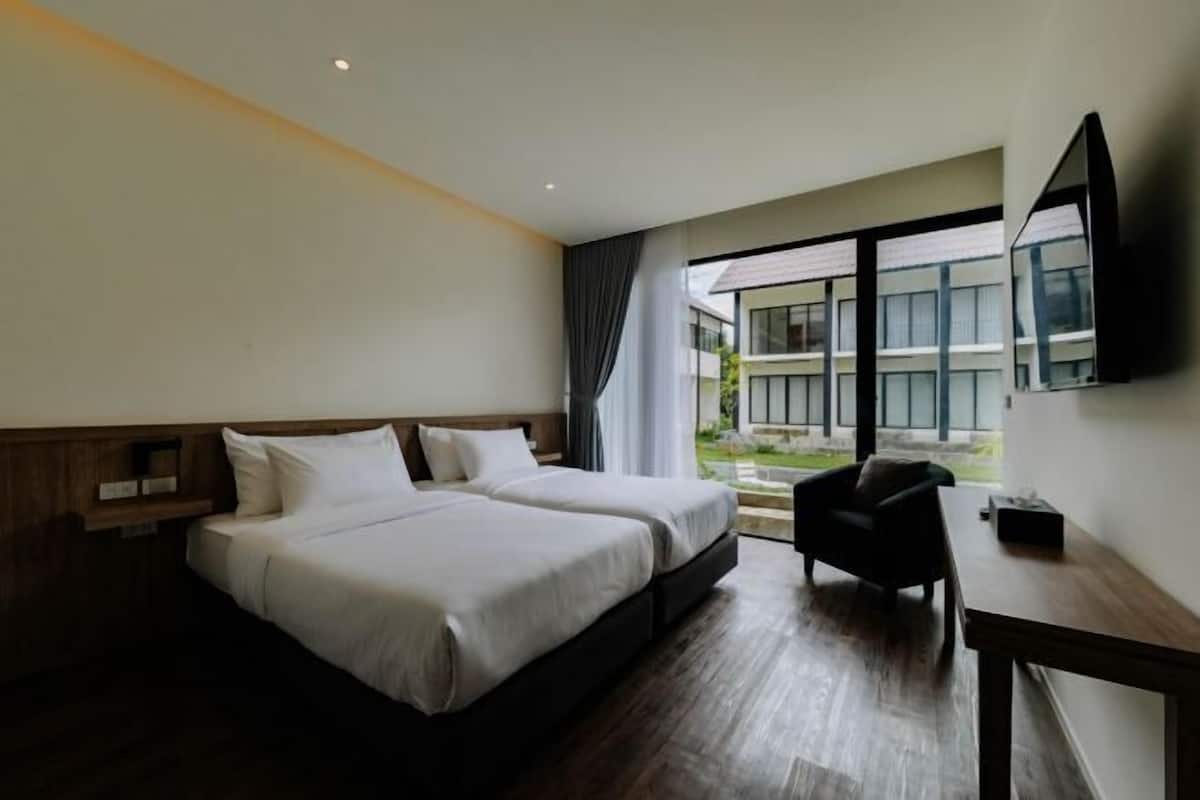 A hotel room with two beds, a desk, and a large window with a view of buildings and greenery.