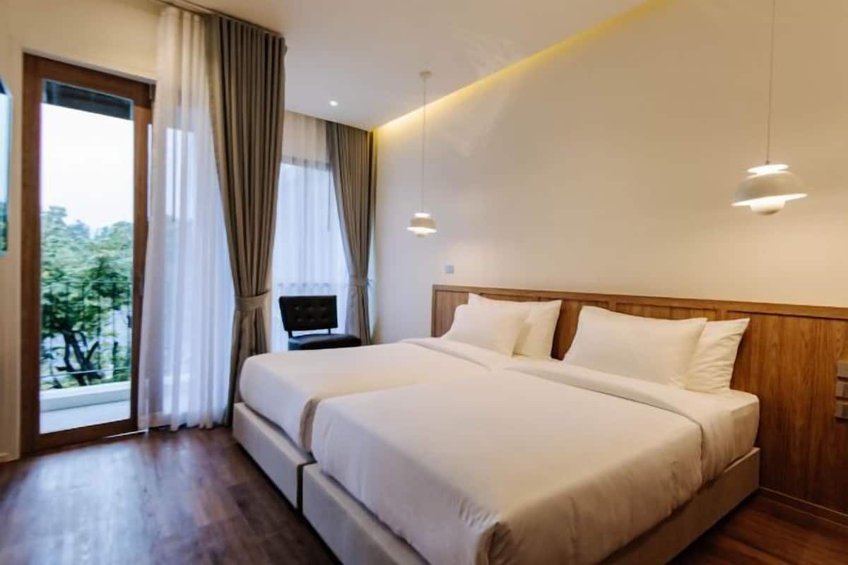 A hotel room with two beds, a wooden headboard, a window with curtains, and a view of trees.