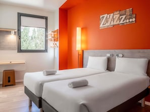 Een hotelkamer met twee bedden, een raam, een kunstwerk aan de muur en een nachtkastje.