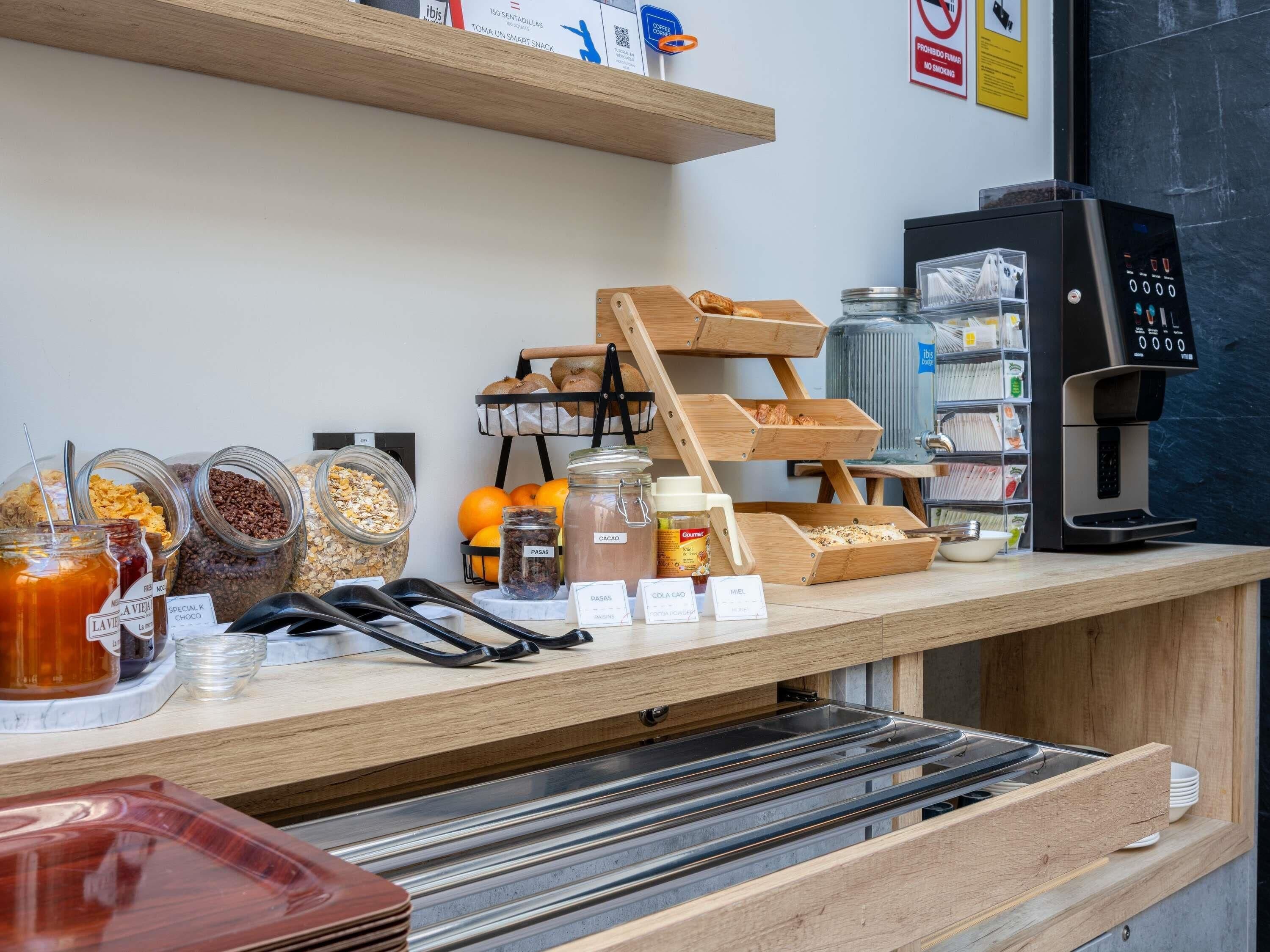 A coffee shop counter with jars of granola, honey, and other spreads, a coffee machine, and a bread display.
