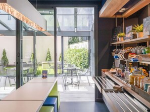 Een modern café met een glazen wand, terras en een ontbijtbalk met diverse producten.