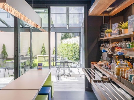 A modern café with a glass wall, outdoor seating, and a breakfast bar with various food items.. ibis budget Madrid Centro Lavapies