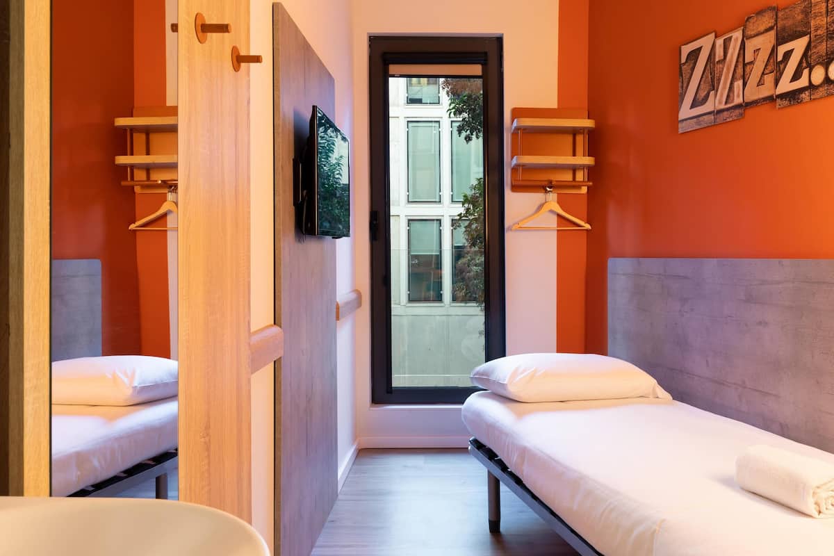 Une chambre d’hôtel avec deux lits, un téléviseur fixé au mur et une fenêtre donnant sur l’extérieur.