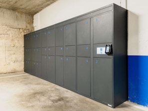 A row of numbered lockers in a utilitarian room with a concrete floor and a blue wall. - ibis budget Madrid Centro Lavapies (Madrid)