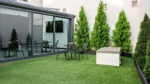 Une terrasse extérieure moderne, dotée d’un gazon synthétique, d’une véranda en verre et de chaises disposées avec soin.
