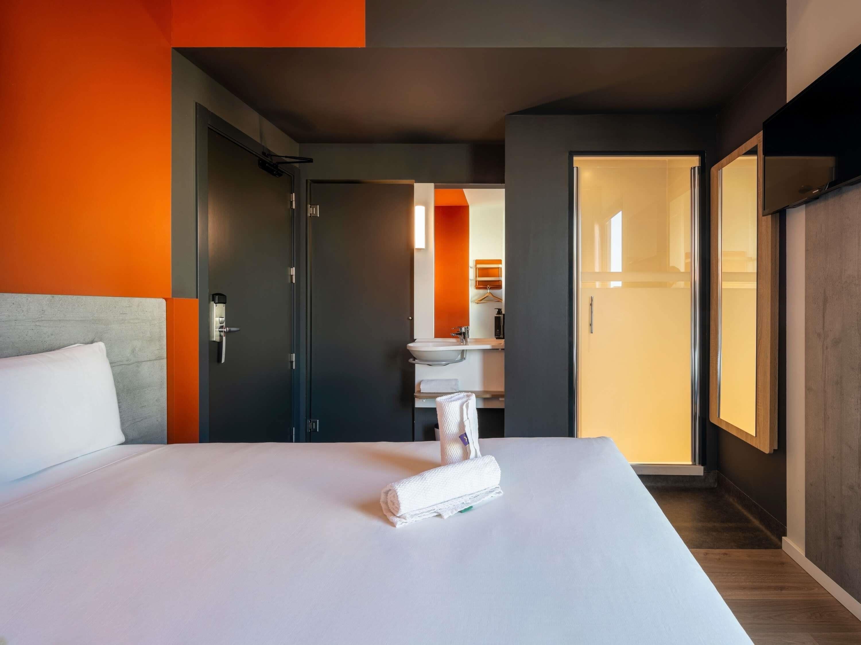 A hotel room with a bed, a bathroom with a sink and mirror, and a wardrobe.
