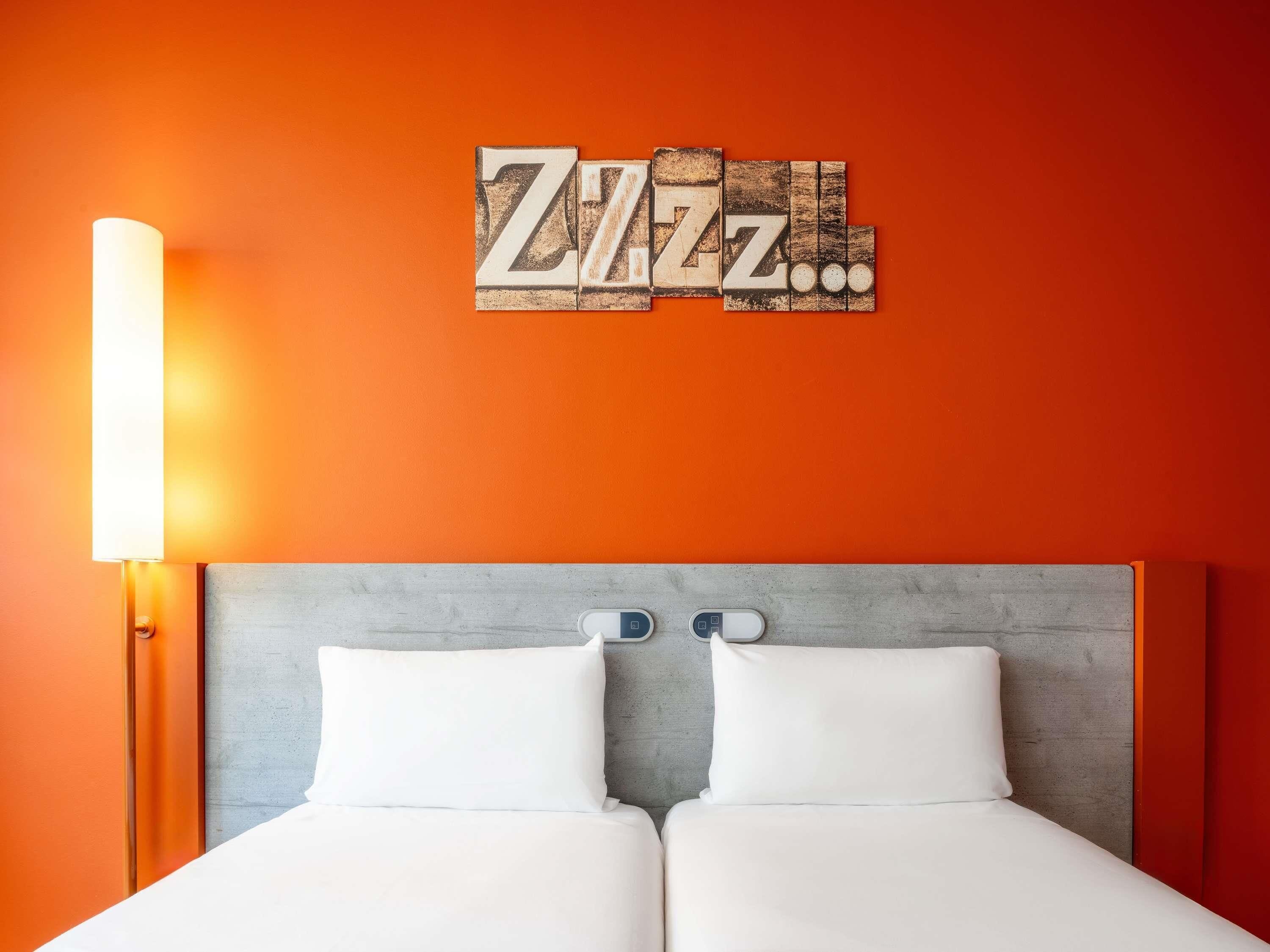 A bed with a grey headboard, white bedding, and a wall-mounted light fixture.
