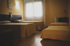 Habitación de hotel con dos camas individuales, una mesita de noche con lámpara, teléfono y ventana con cortinas ligeras.