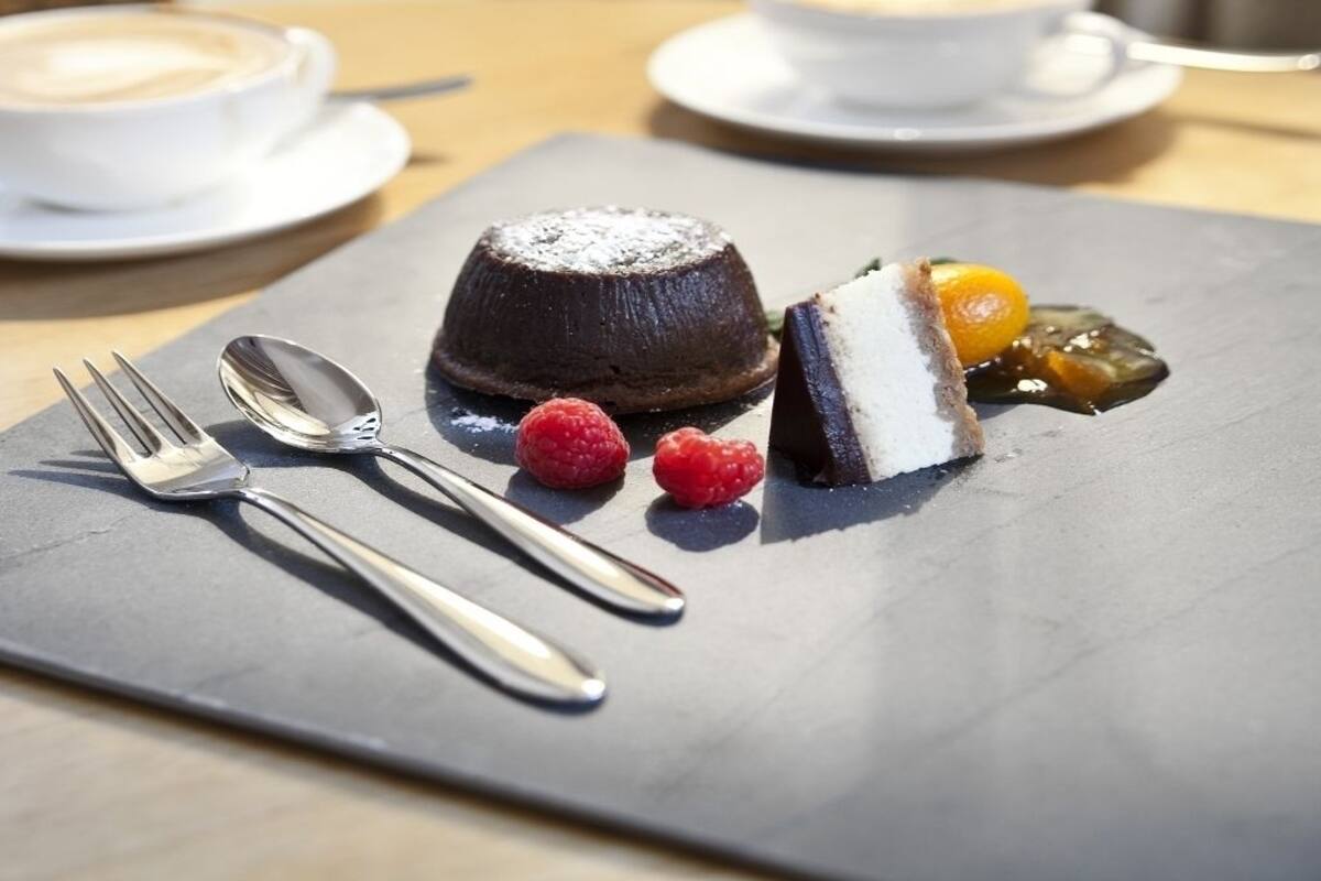 A dessert plate with a chocolate lava cake, raspberries, and a slice of cake with a yellow fruit on a slate board.