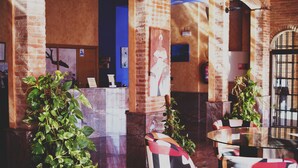 A lobby with brick walls, a reception desk, and a statue. There are chairs and a table with a glass top. - Hotel Restaurante La Bodega (La Almunia de Dona Godina)