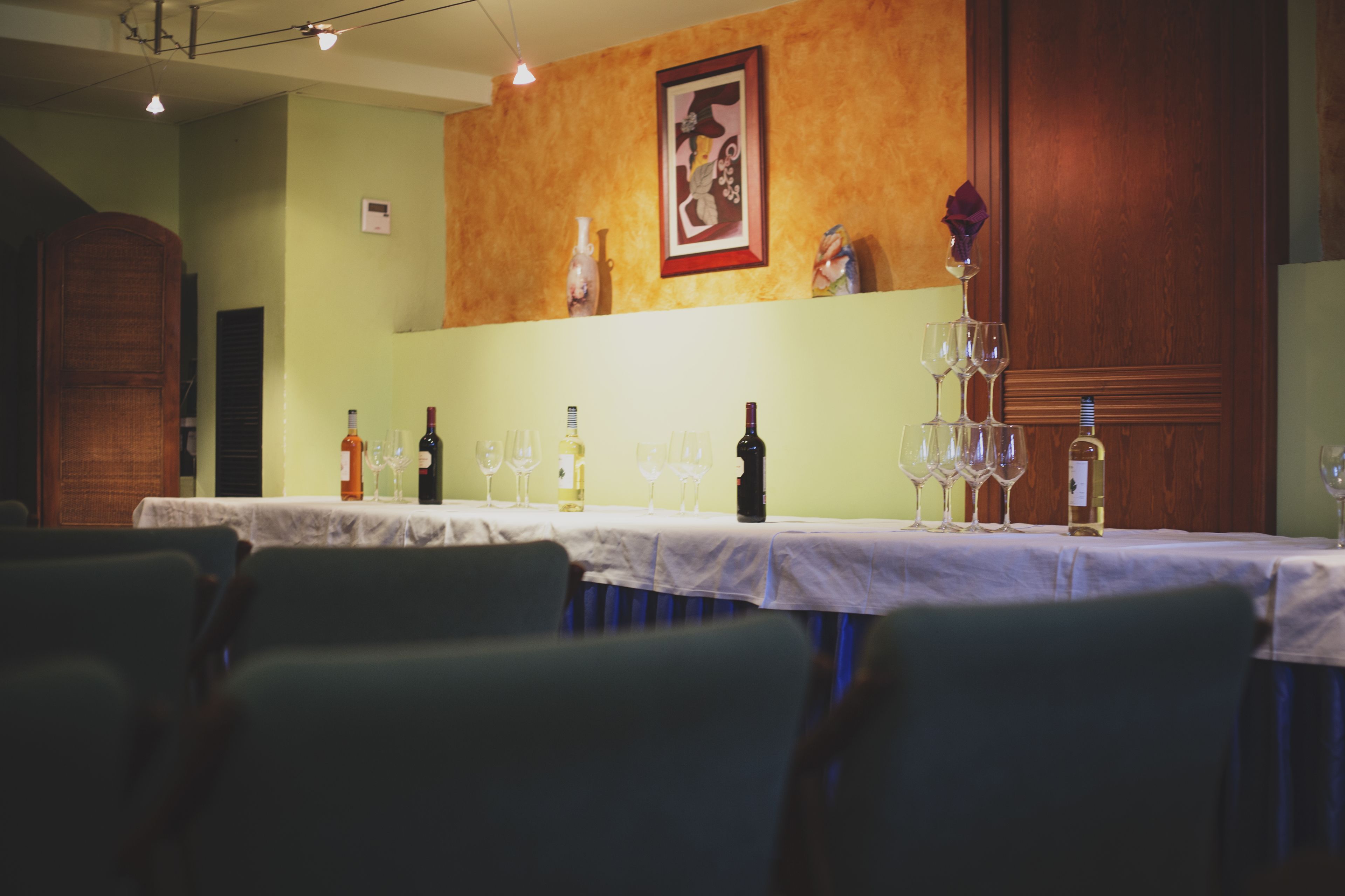 Un restaurante con una mesa larga preparada para comer, copas de vino y botellas.