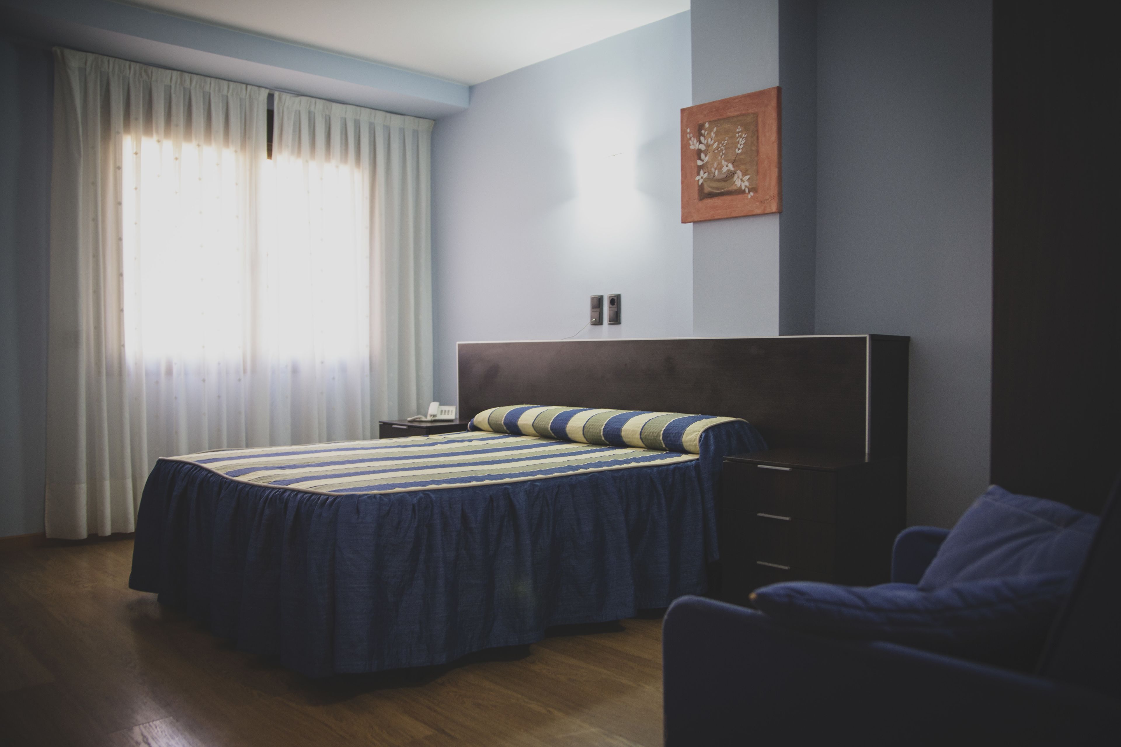 A bedroom with a bed, a chair, a nightstand, and a wall-mounted picture.