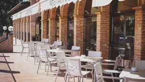 An outdoor cafe with white tables and chairs, a brick building, and a sign that reads "RESTAURANTE". - Hotel Restaurante La Bodega (La Almunia de Dona Godina)