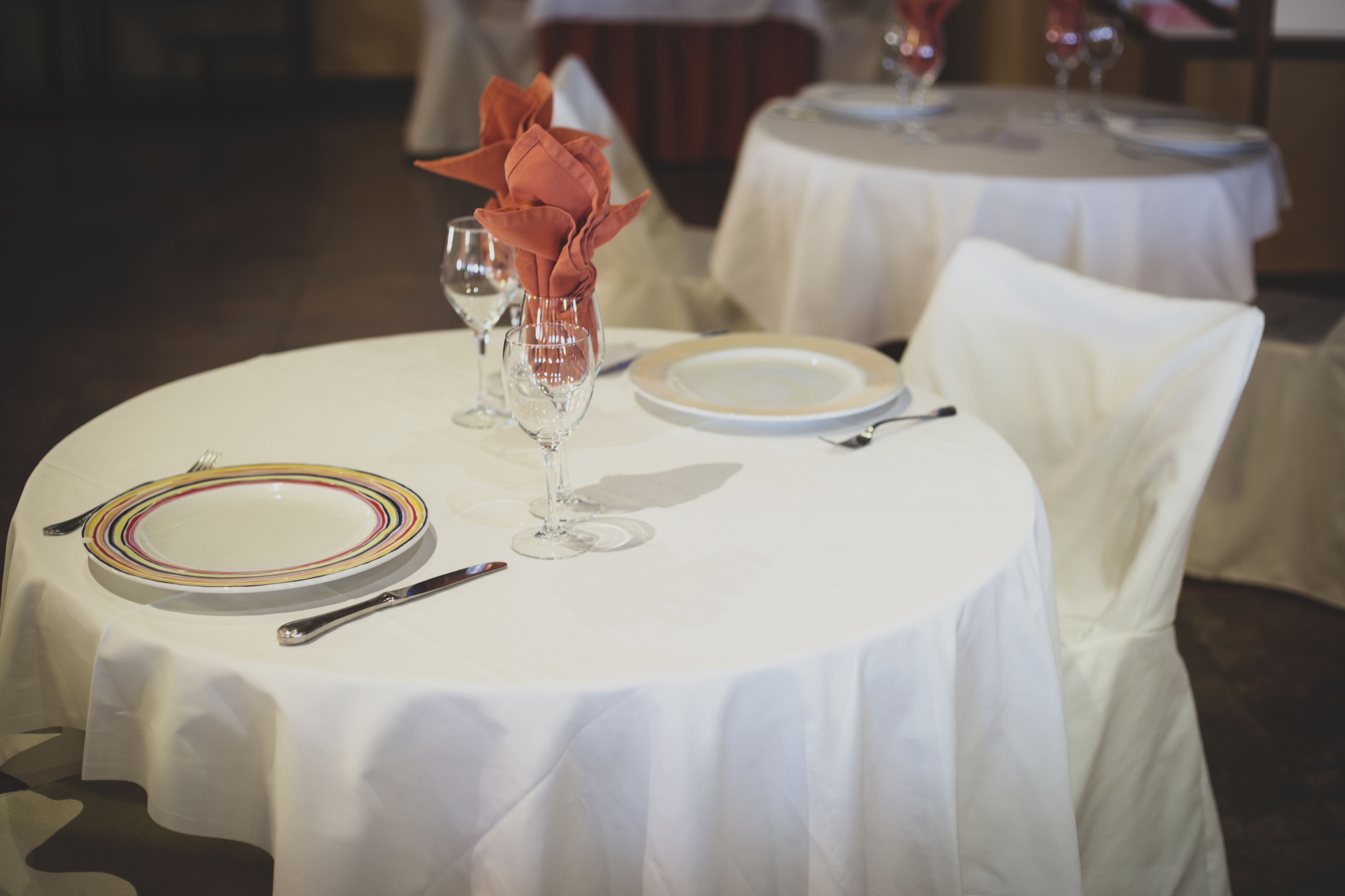 Una mesa de comedor redonda con mantel blanco, servida con platos, cubiertos y copas de vino.