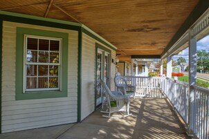A covered porch with white wicker rocking chairs and a wooden ceiling.