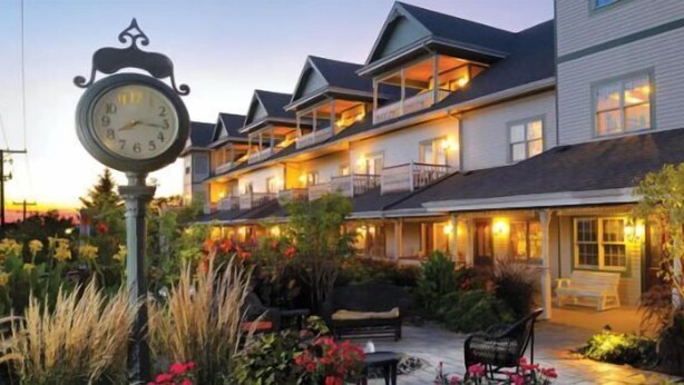 A multi-story hotel with a porch area, outdoor seating, and a clock. - Carlisle Inn Walnut Creek (Millersburg)
