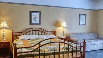 A neatly made bed with a quilt, two bedside lamps, a bedside table, a gray sofa, and two framed floral pictures on the wall.